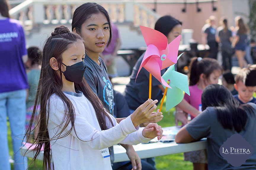 Students teach visiting children and families how to make pinwheels.